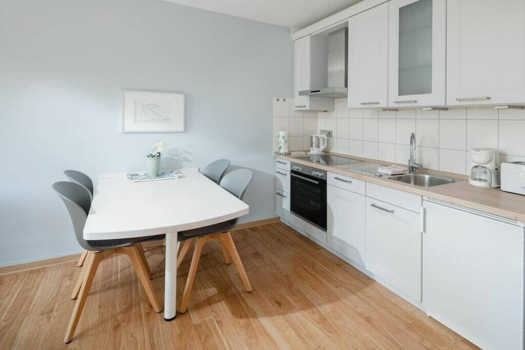 A modern kitchen with white cabinets, a white countertop, and a dining table with chairs.
