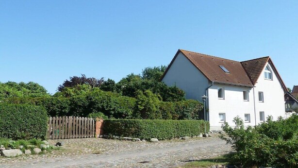 Ein zweistöckiges Haus mit geneigtem Dach, einer gepflasterten Auffahrt und einem Holzzaun.