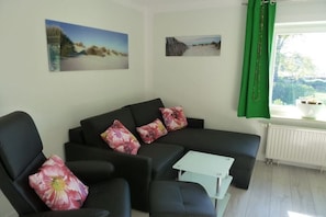 Ein Wohnzimmer mit einem schwarzen Sofa, floralen Kissen, einem kleinen weißen Tisch und zwei Bildern an der Wand.