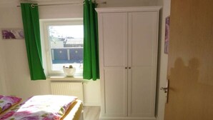 Ein Schlafzimmer mit einem Bett, einem weißen Kleiderschrank, einem Fenster mit grünen Vorhängen und einer Heizung.