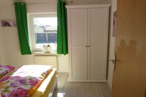 Ein Schlafzimmer mit einem Bett, einem weißen Kleiderschrank, einem Fenster mit grünen Vorhängen und einer Heizung.