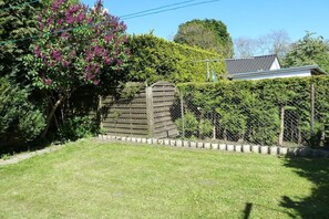 Un jardin clos, avec une porte en bois, une pelouse verdoyante et une maison en arrière-plan.