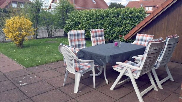 Eine Terrassengruppe mit Tisch und Stühlen, umgeben von einem Hecken und einem Holenzaun.
