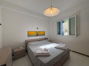 A bedroom with a bed, bedside tables, a hanging light fixture, a window with blinds, and a painting on the wall. - La Casa dei Melograni (Marina Di Ragusa)