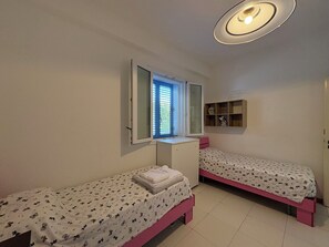 A small, well-lit room with two single beds, a desk, and a window with blinds. - La Casa dei Melograni (Marina Di Ragusa)