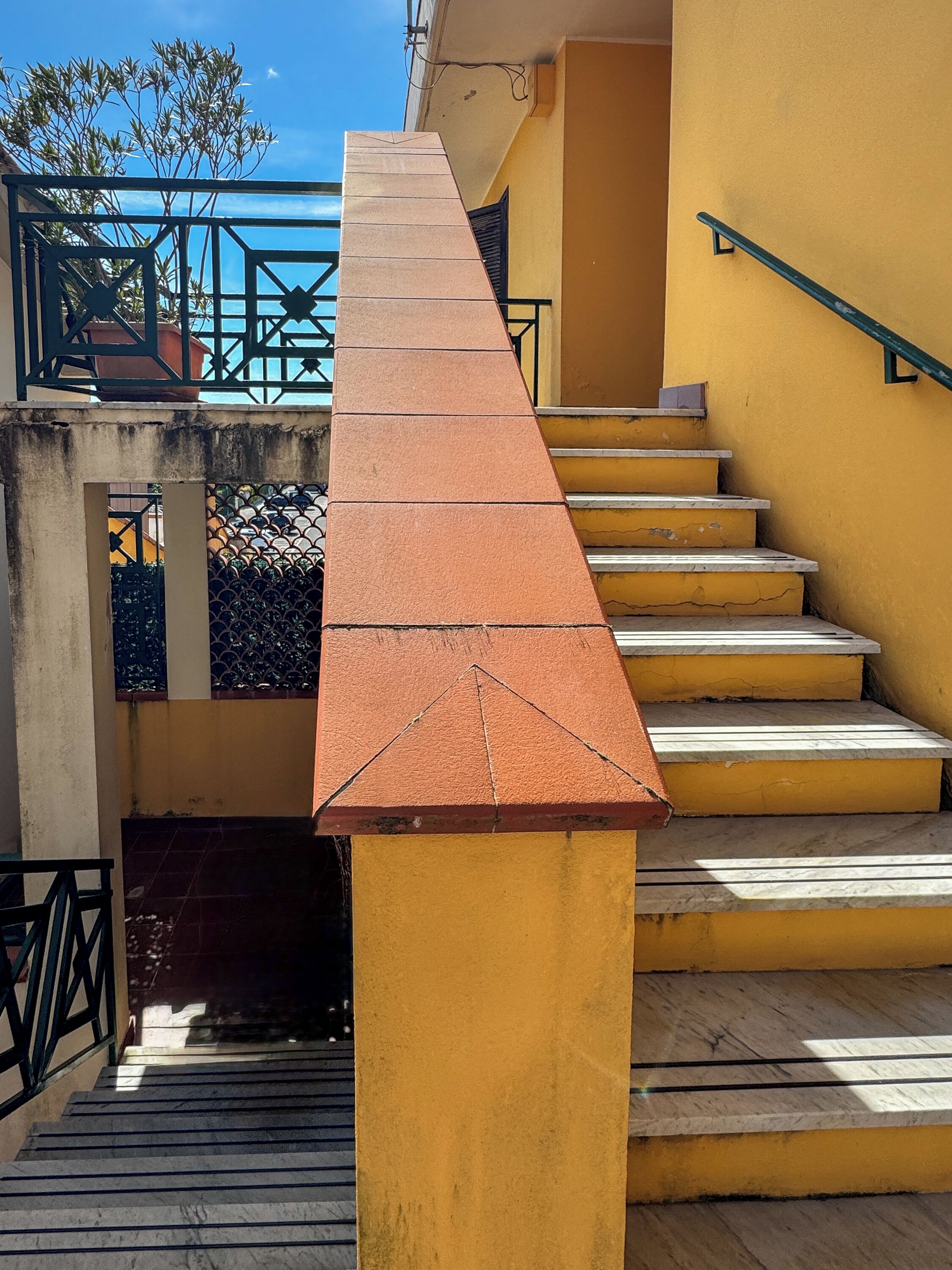 A staircase with a red handrail leading to a landing, surrounded by yellow walls and a metal railing.