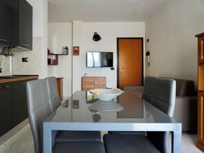 Eine moderne Küche mit Einbauherd, ein Essbereich mit Glastisch und Ledersesseln, ein flachbildfernseher an der Wand und eine Holztür.