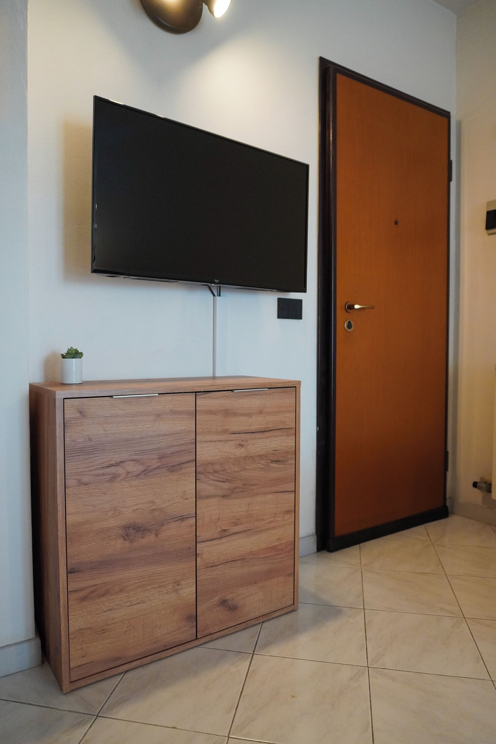A room with a wooden cabinet, a flat-screen TV mounted on the wall, and a closed wooden door.