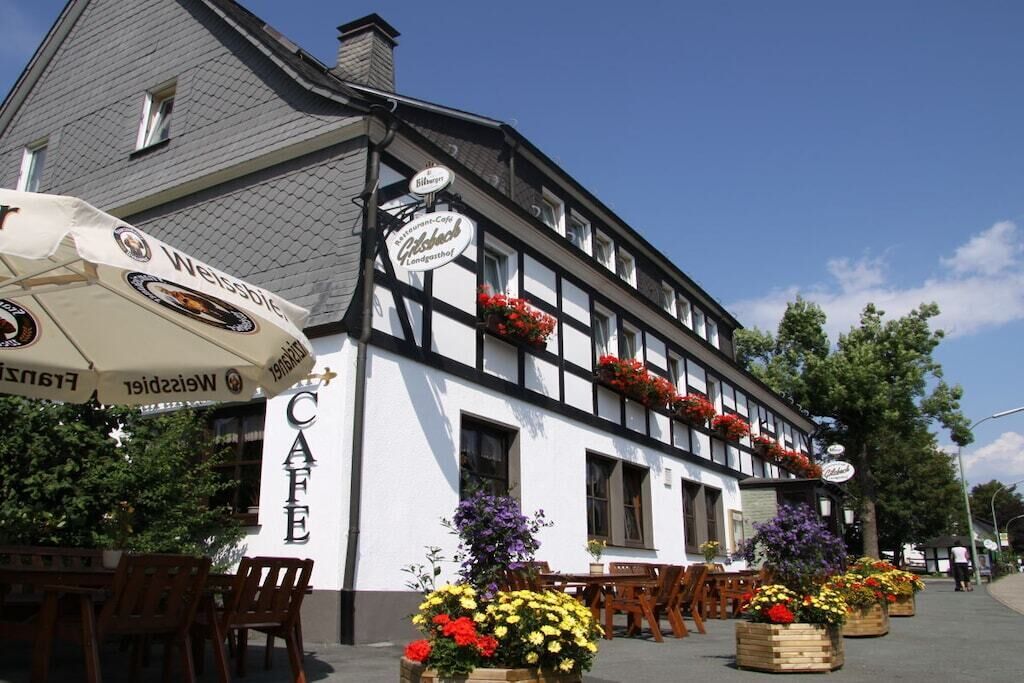 Een gebouw in traditionele Europese stijl met een cafébord, terrasplekken en bloempotten.