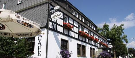 A traditional European-style building with a cafe sign, outdoor seating, and flower planters.