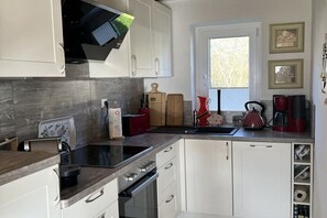Eine moderne Küche mit weißen Schränken, einem eingebauten Backofen und einem Fenster für natürliches Licht.