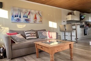 Ein Wohnzimmer mit einer Couch, einem Glastisch und einem Bild von Segelbooten an der Wand.