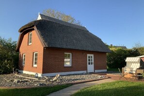 Ein Backsteinhaus mit einem Strohdach, einer Haustür und einer kleinen Veranda.