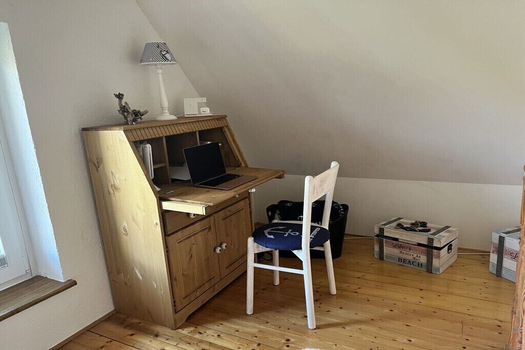 A small room with a wooden desk, a laptop, a white chair, a lamp, and a window.