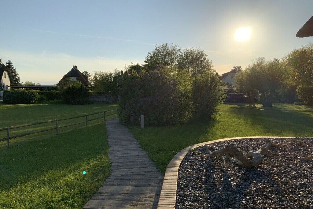 Un sentier traverse une zone herbeuse, bordée d’une clôture en bois d’un côté et d’un mur de pierre de l’autre, sous un ciel dégagé.