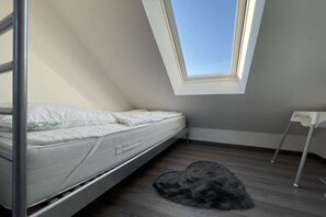 Ein Zimmer mit einem Bett, einem Dachfenster, einem kleinen Tisch und einem flauschigen Teppich.