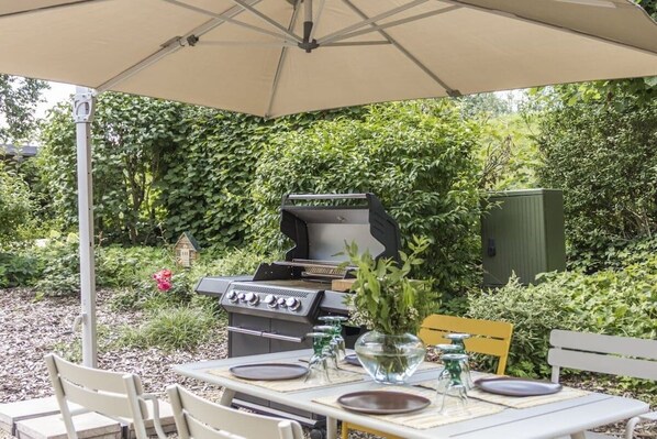 Ein Essbereich im Freien mit Grill, Tisch gedeckt mit Tellern und einer Bank.