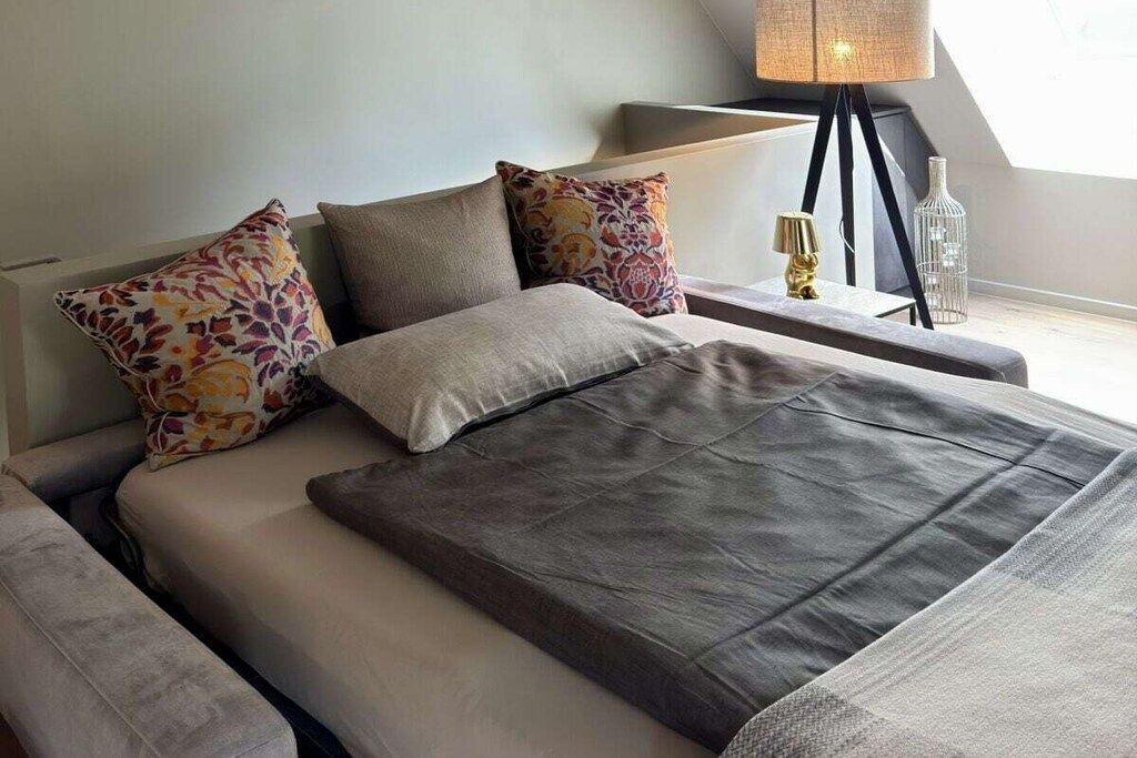 A modern bedroom with a bed, pillows, a bedside table with a lamp, and a decorative bottle.