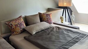 Een moderne slaapkamer met een bed, kussens, een nachtkastje met een lamp en een decoratieve fles.