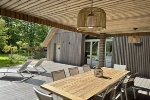 An outdoor dining area with a wooden table and chairs, a hanging light fixture, and a view of a building with vertical siding. - Holiday home in Oberndorf with barbecue (Oberndorf)