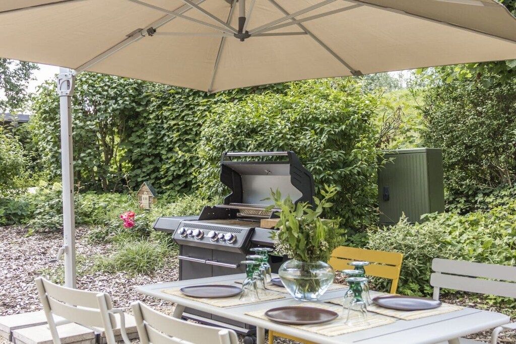 Un espace extérieur aménagé pour les repas, avec un barbecue, une table dressée et un banc.