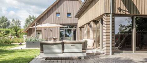 Una casa moderna con fachada de madera, un patio con un sofá blanco y un ventanal que da a una terraza.