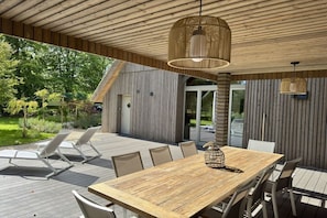Eine Terrasse aus Holz mit Esstisch und Stühlen, umgeben von einem Holzzaun und viel Grün.