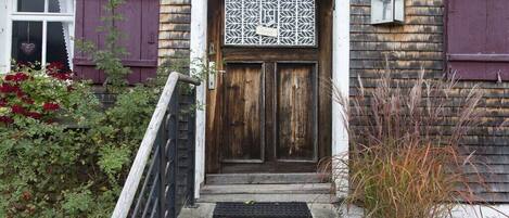 A wooden door with a decorative panel, a small porch with steps, and a metal railing.