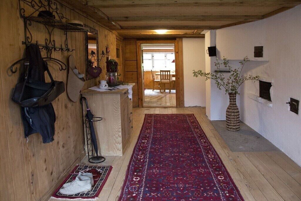 A wooden interior with a red patterned rug, a horse saddle, and a stable door leading to an outdoor area.