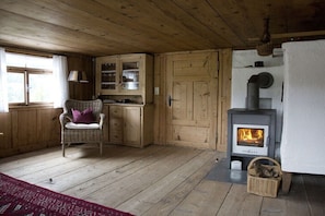 A wooden interior with a fireplace, a wicker chair, and a window with curtains. - Hut "Behind" the Mountain (Hittisau)