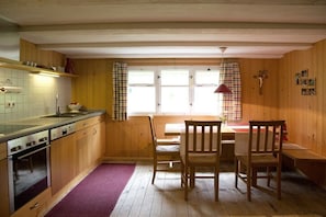 A kitchen with wooden cabinets, a sink, and a dining area with a table and chairs. - Hut "Behind" the Mountain (Hittisau)