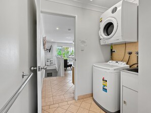 Un espace buanderie équipé d’un lave-linge, d’un sèche-linge et d’une planche à repasser.