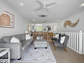 A modern living room with a grey sofa, ottoman, and armchair, a dining area with a wooden table and chairs, and a kitchen in the background. - Sails On Horseshoe Apartment 10 (Horseshoe Bay)