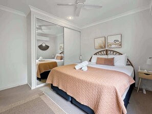 A hotel room with a bed, a bedside table, a mirror, and a ceiling fan. - Sails On Horseshoe Apartment 10 (Horseshoe Bay)