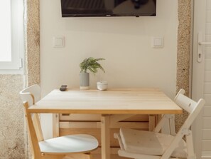 Ein Holztisch mit vier Stühlen, einem Blumentopf, einer Fernbedienung und einer weißen Tasse darauf.