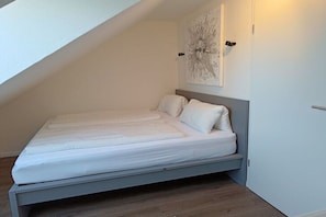 Ein Einzelbett mit Kopfteil in einem Zimmer mit geneigten Decken.