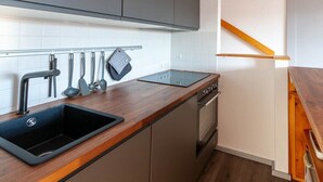 Una cocina con un lavamanos negro, encimera de madera y electrodomésticos de acero inoxidable.