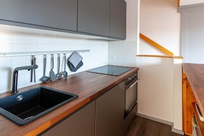 Eine Küche mit einem schwarzen Spülbecken, einer Holzausziehtafel und Edelstahlgeräten.