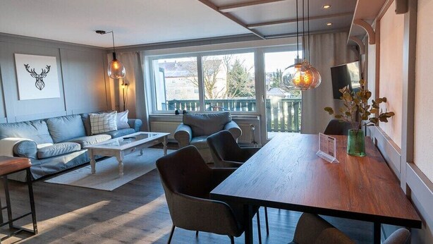 Una sala de estar moderna con sofá, mesa de centro y mesa de comedor. Hay un ventanal con vistas al exterior.