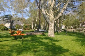 Ein Park mit einem großen Baum, einer Holzbrücke und einer Skulptur.