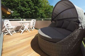Ein Korbsessel mit Baldachin, ein kleiner Tisch und Stühle auf einer Holzterrasse.