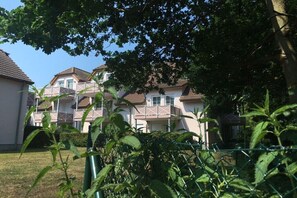 Ein Wohngebäude mit mehreren Balkonen, blauem Himmel und einem eingezäunten Gartenbereich.
