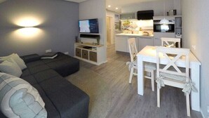 A modern living room with a sofa, a dining table with chairs, and a kitchen area with a microwave and oven. - Holiday apartment with 1 bedroom (Dierhagen)