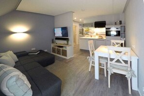 Ein modernes Wohnzimmer mit einer Couch, einem Esstisch mit Stühlen und einer Küchenzeile mit Mikrowelle und Backofen.