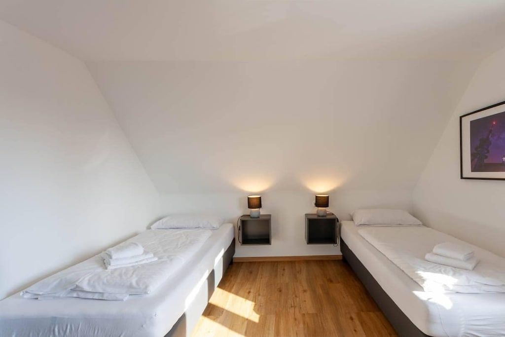 Una habitación con dos camas individuales, piso de madera y dos lámparas de noche.