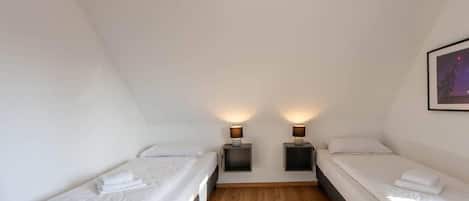 Una habitación con dos camas individuales, piso de madera y dos lámparas de noche.