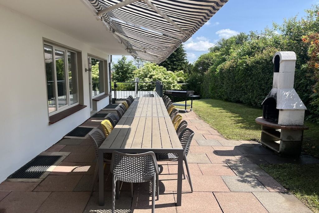An outdoor patio with a long wooden table and chairs, a grill, and a covered seating area.