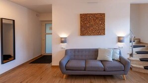 Een moderne woonkamer met een grijze bank, een abstract kunstwerk aan de muur, en een trap aan de rechterkant.