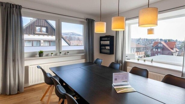 Een vergaderruimte met een grote tafel, stoelen en hanglampen.