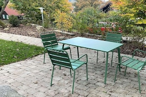 Eine Terrasse mit einem grünen Metalltisch und -stühlen, umgeben von Bäumen und einem Steinweg.